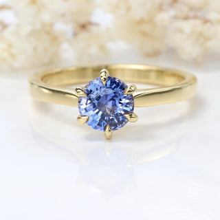 Natural unheated lavender sapphire solitaire engagement ring photographed on soft floral background.