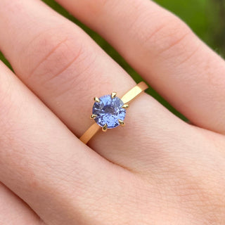 Lavender blue sapphire solitaire engagement ring in 18ct gold shown worn on hand.