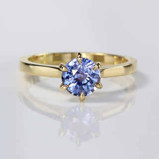 Handmade 18ct gold lavender blue sapphire solitaire engagement ring on reflective surface.