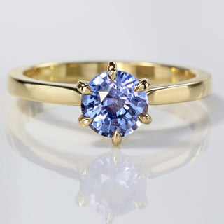Handmade 18ct gold lavender blue sapphire solitaire engagement ring on reflective surface.