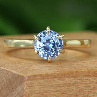 Lavender blue sapphire solitaire engagement ring photographed on wooden surface.
