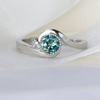 Macro close-up of teal Parti sapphire bezel set in platinum with milgrain detail and pear diamond accent.