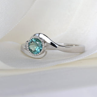 Platinum wave engagement ring with teal Parti sapphire and diamond accent showing flowing band shape.