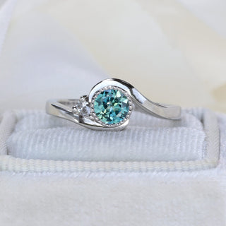 Natural unheated teal Parti sapphire in platinum wave setting with pear cut diamond accent.
