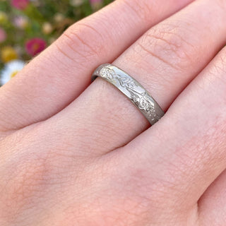 Platinum court wedding ring with hand engraved oak leaves and acorns around the 4mm wide band. Show here being worn on the hand.