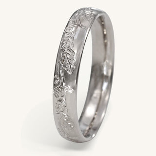 Platinum 4mm court wedding band with hand engraved oak leaves on the band resting on a white surface
