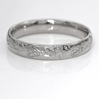 4mm court platinum wedding ring with oak leaf pattern engraved on the band resting on a white surface