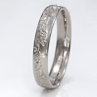Platinum 4mm court wedding band with hand engraved oak leaves on the band resting on a white surface