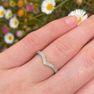 Hand engraved 950 platinum wishbone wedding ring with orange blossom flowers and leaves around the band, framed by a milgrain border. Shown being worn on the hand