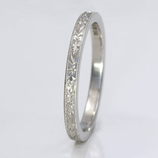 Platinum 2mm wedding band with hand engraved orange blossom pattern, resting on a white surface