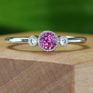 Platinum trilogy engagement ring with pink sapphire photographed against green background
