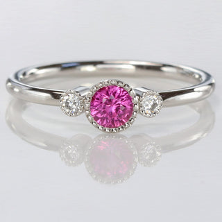 Pink sapphire petite platinum engagement rings with diamonds on a reflective background