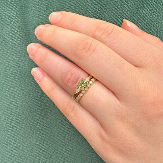 Green sapphire and diamond trilogy engagement ring and diamond wedding ring worn on the hand with green fabric background