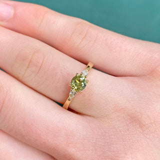 Green sapphire and diamond trilogy ring worn on the finger with green background