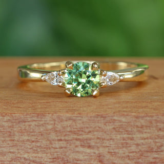 Green sapphire and pear cut diamond engagement ring  on wooden box with blurred green background