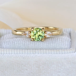 Pale green sapphire and pear cut diamond trilogy engagement ring on a grey cushion