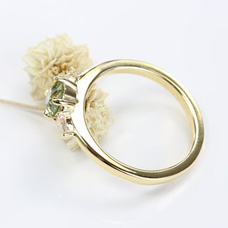 Side view of 18ct gold green sapphire and diamond trilogy ring resting on a cream flower on a white surface