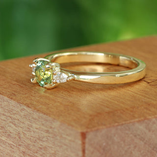 Side view of green sapphire and pear cut diamond trilogy engagement ring on a wooden box with blurred green background