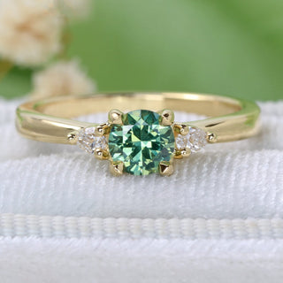 18ct gold green sapphire engagement ring with pear cut diamonds on a white velvet box