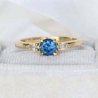 Handmade 18ct gold royal blue sapphire trilogy ring photographed on pale textured fabric.