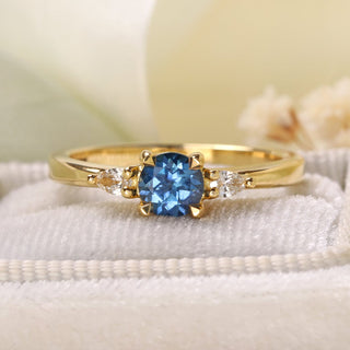 18ct gold sapphire and pear cut diamond trilogy engagement ring on a felt ring box. Green ribbon and floral background.