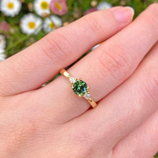 Handmade 18ct sapphire and diamond trilogy engagement ring set with a fair trade dark green sapphire and pear cut natural white diamonds. Displayed on the hand.