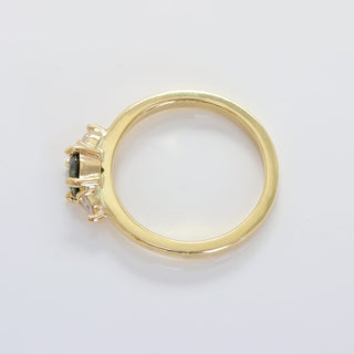 View of the top of the handmade trilogy engagement ring set with a fair trade dark green sapphire and pear cut diamonds, on a grey background.