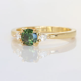 Angled view of 18ct gold green sapphire and diamond trilogy engagement ring on a reflective surface