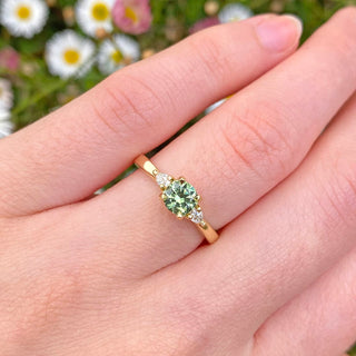 18ct sapphire and diamond trilogy engagement ring set with a fair trade green sapphire and pear cut natural white diamonds. Displayed on the hand.
