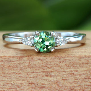 Green sapphire trilogy engagement ring in platinum photographed on Lilia Nash branded wooden box.