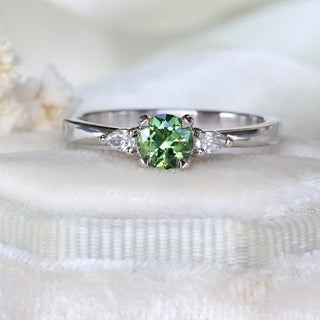 Handmade green sapphire trilogy engagement ring on felt box with white flowers.
