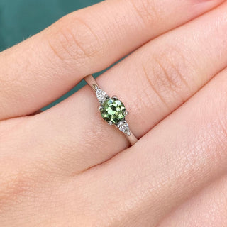 Platinum green sapphire trilogy engagement ring shown worn on hand.