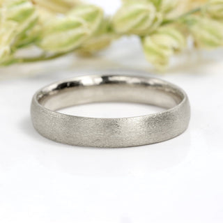 4mm court shape platinum wedding ring with spun silk finish, on white surface with flower buds
