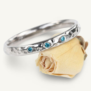Handmade sustainable 950 platinum hammered wedding band set with blue diamonds, resting against a rose flower