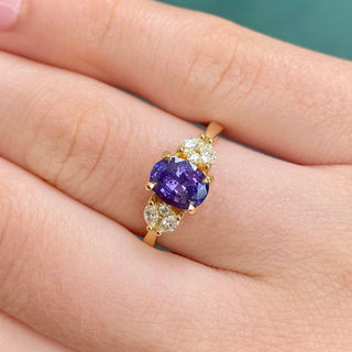 Oval purple sapphire and diamond engagement ring shown worn on hand.