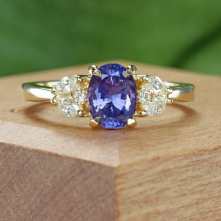 Handmade oval purple sapphire cluster engagement ring on wooden box with green background.
