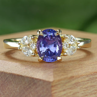 Handmade oval purple sapphire cluster engagement ring on wooden box with green background.