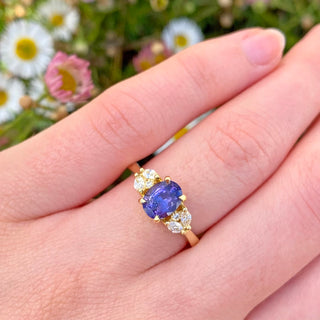One of a kind 18ct gold engagement ring set with a 1.31 carat oval purple sapphire with marquise and round natural side diamonds. Worn on the hand with daisy backdrop