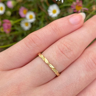 Handmade wedding band with engraved leaves at the front of the band. Made from sustainable solid 18ct gold and displayed being worn on the hand with daisies in the background