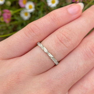 Sustainable 950 platinum wedding band with hand engraved leaves at the front. Shown being worn on the finger with daisy backdrop
