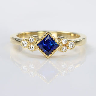 Handmade 18ct gold princess cut sapphire and diamond cluster ring with milgrain detail.