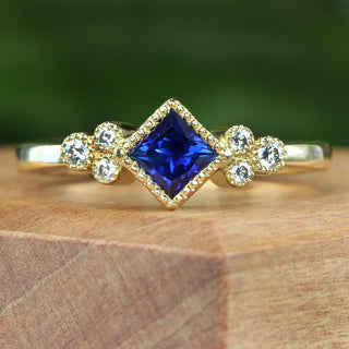 18ct gold princess cut blue sapphire and diamond cluster ring displayed on wooden surface.