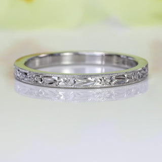Close-up of the slim platinum wedding ring showing the engraved floral pattern framed by a milgrain border.