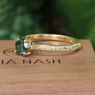 Side view showing the hand engraved orange blossom pattern on a solitaire 18ct gold engagement ring set with a green sapphire