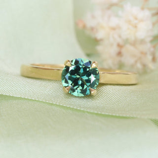 Parti sapphire solitaire engagement ring with teal and green sapphire photographed on green ribbon and white flowers