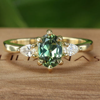 18ct gold trilogy engagement ring with an oval green sapphire and pear cut side diamonds on a Lilia Nash branded wooden box