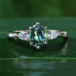 18ct gold oval fair trade green sapphire and pear cut diamond trilogy engagement ring on a leaf
