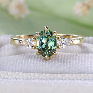 18ct gold trilogy engagement ring with an oval green sapphire and pear cut side diamonds on a white velvet box