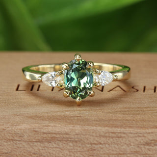 18ct gold trilogy engagement ring with an oval green sapphire and pear cut side diamonds on a Lilia Nash branded wooden box