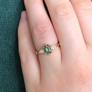 18ct gold trilogy engagement ring set with an oval green sapphire and pear cut diamonds, being worn on the hand